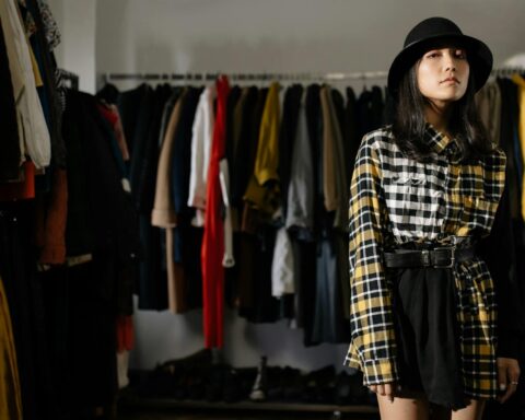 A Woman Wearing Plaid Long Sleeves Shirt and Black Skirt Standing Near Clothes Rack while Looking at the Camera